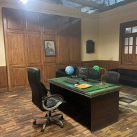 Senior officer cabin with green-topped desk, office chairs, sofa and wood-panelled walls at Bhajanlal Estate