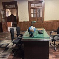 Front view of government officer cabin with desk globe, office chairs and wooden doors in Stage 04 set