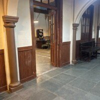 Side corridor view with arched pillars, open wooden doors and bench seating in office set at kaman